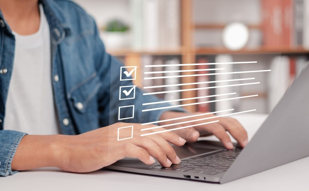 Woman in jean jacket from the neck down working on a silver laptop doing an IRS WISP review for her tax firm.
