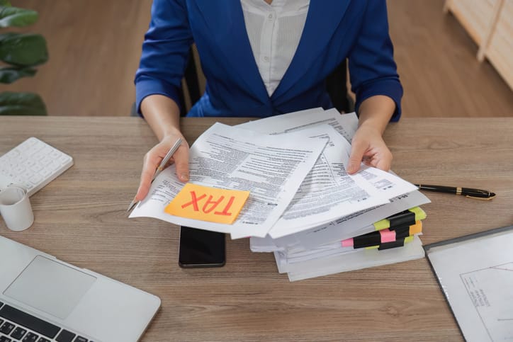 A female tax pro in a blue sweater sifting through paper WISP documentation with an orange post it note on top.