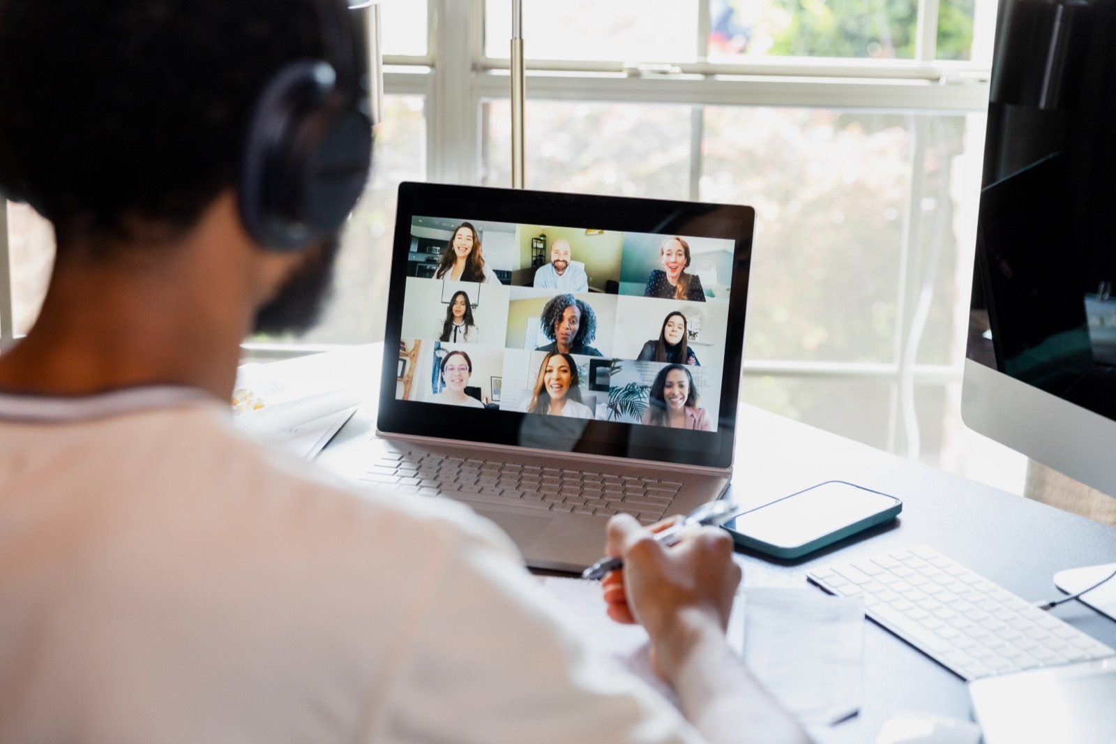 A man wearing headphones taking part in a virtual meeting on his laptop, with several other participants visible on screen